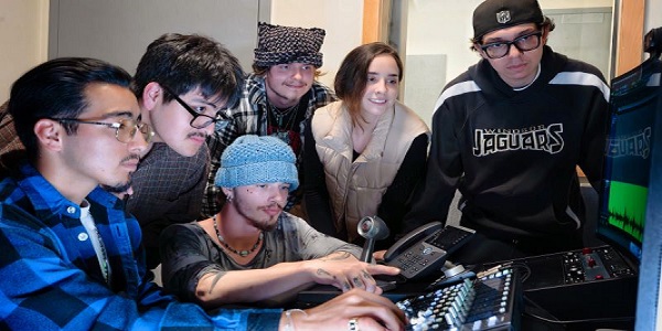 Students collaborating in a recording studio control room, learning audio mixing and sound engineering using professional equipment.